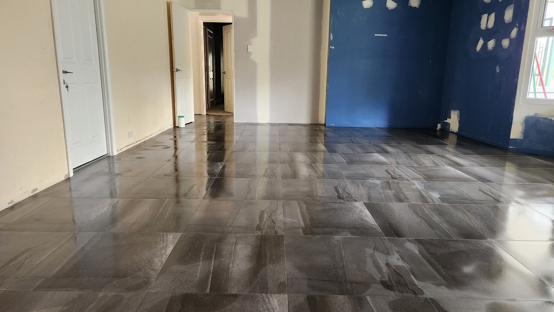 A dark grey marble-look tiled floor running through a room and out into a hallway