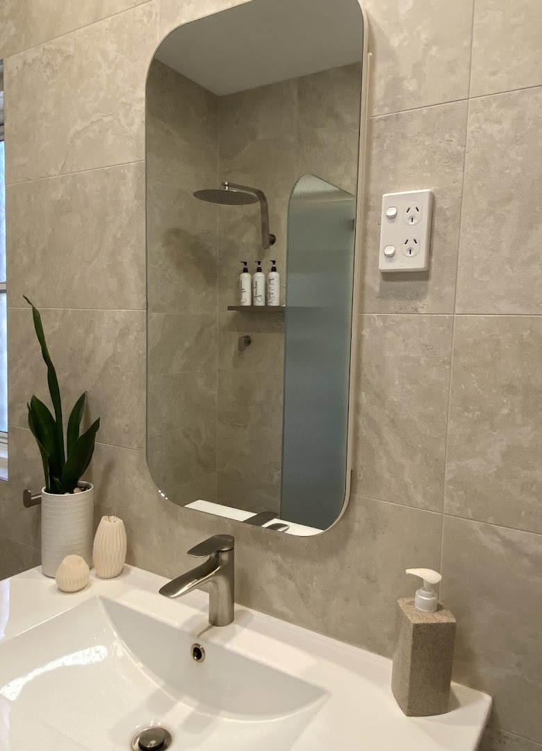 A bathroom vanity and mirror against a wall tiled in warm marble-look porcelain