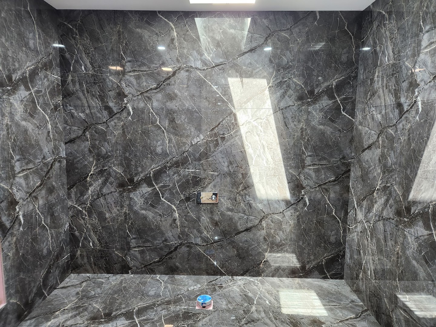 A shower wall tiled in large charcoal marble-look porcelain with a fine dark grout line
