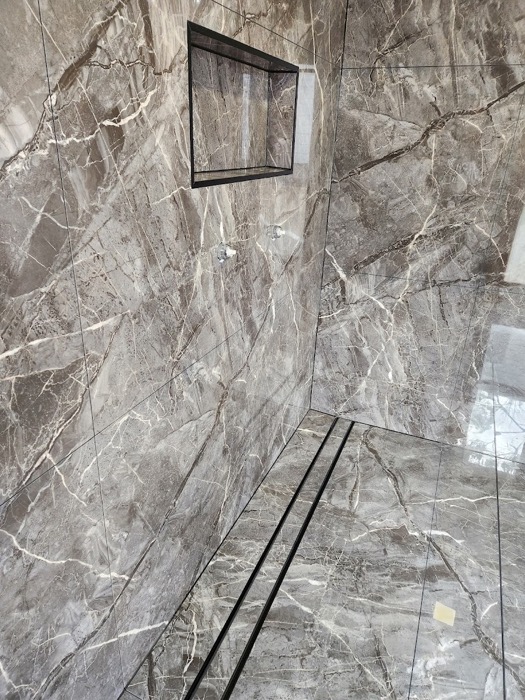A shower recess tiled in grey marble-look porcelain with a linear floor drain