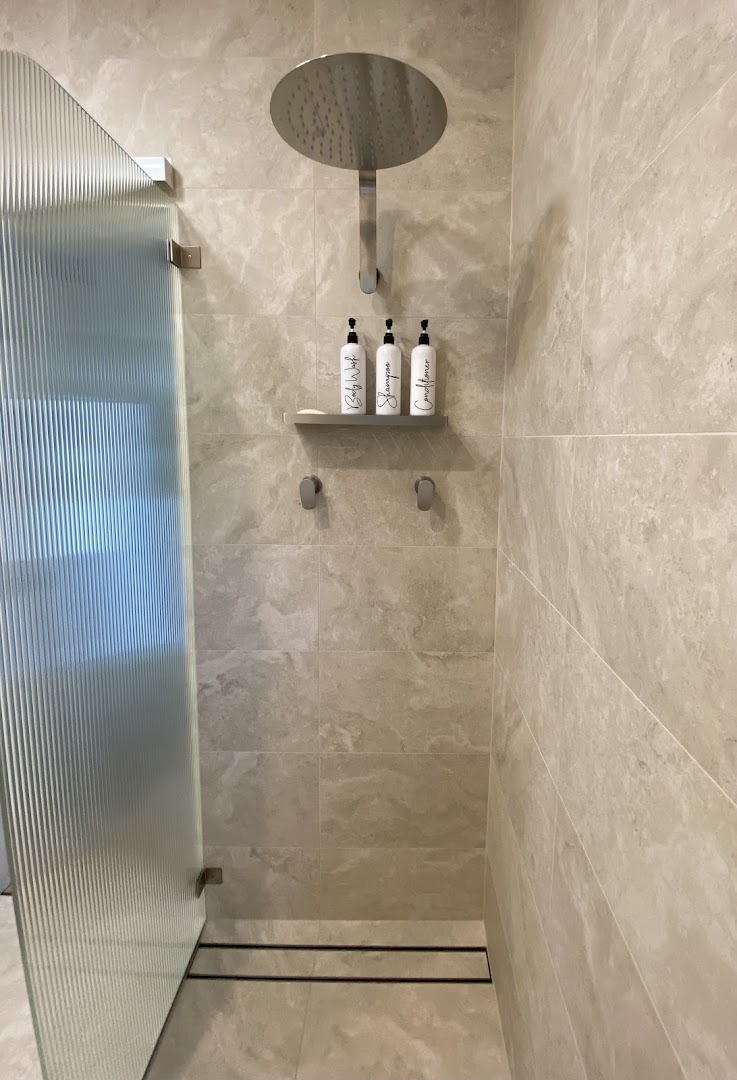 A shower recess tiled floor to ceiling in warm marble-look porcelain behind a glass screen