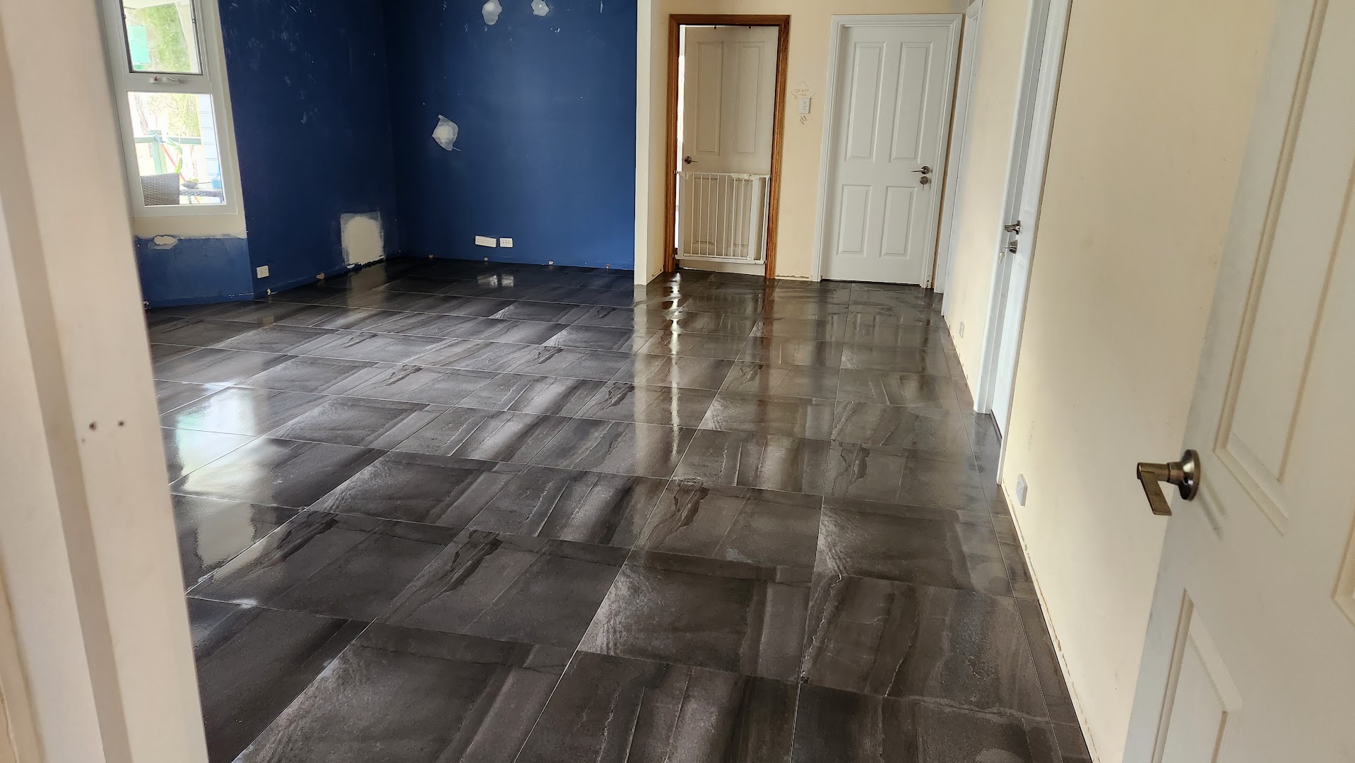 A dark grey marble-look tiled floor laid through a room with a deep blue painted wall