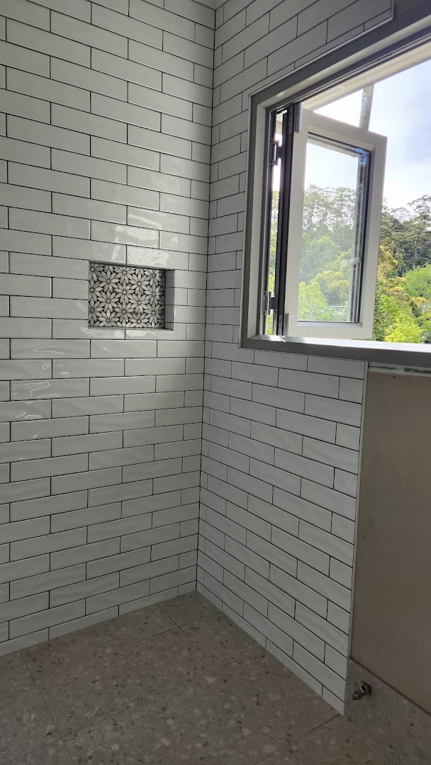 A shower wall tiled in white brick tiles with a recessed shelf beside a window