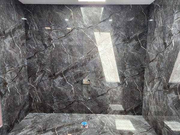 A shower wall tiled in large charcoal marble-look porcelain with a fine dark grout line