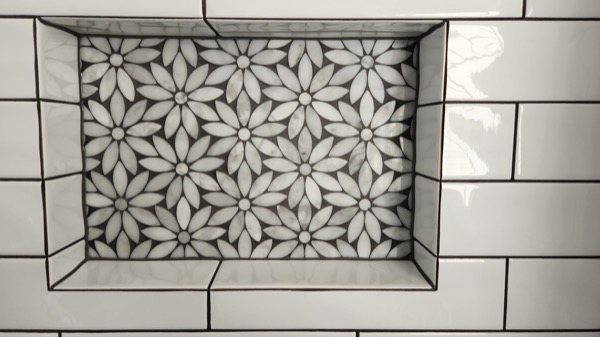 A floral mosaic panel set into a white brick-tiled floor and framed by border tiles
