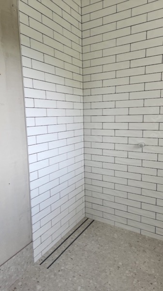 A shower recess lined in white brick tiles with a dark grout line
