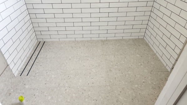 A shower base and white brick-tiled walls with a linear drain along one edge