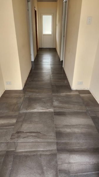 A hallway floor laid in grey concrete-look tiles running to the front door