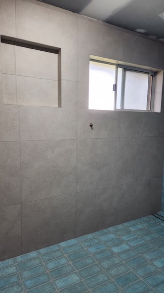 A part-tiled wall in large grey tiles beside a window opening, mid job