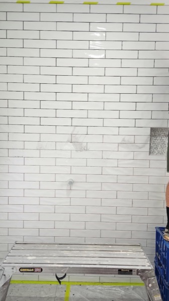 A white brick-tiled wall with a trestle standing in front of it, mid job