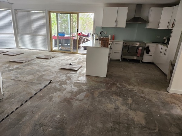 A kitchen and living area floor stripped back with tiles laid out ready