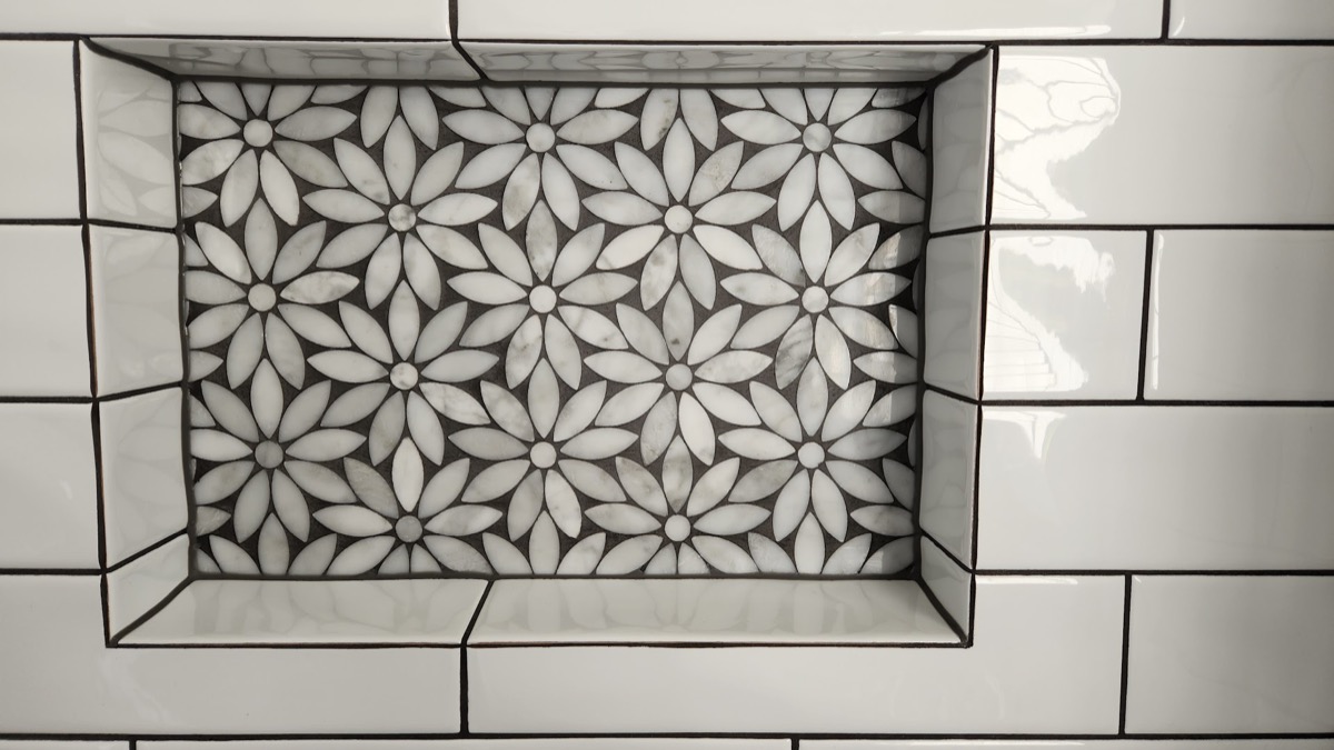 A floral mosaic panel set into a white brick-tiled floor and framed by border tiles