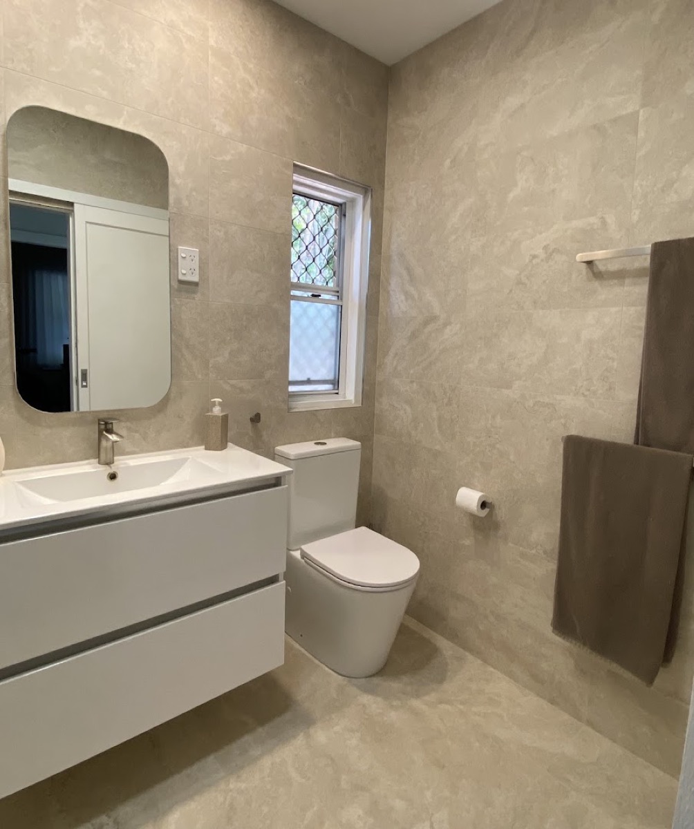 A finished bathroom with a vanity, toilet and warm limestone-look wall tiles