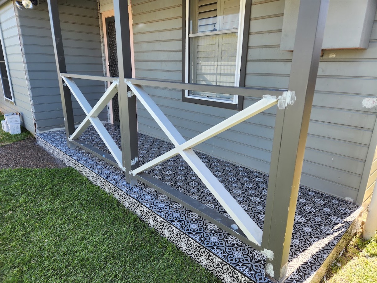 Patterned tiles laid along an outdoor edge beside a weatherboard wall and lawn